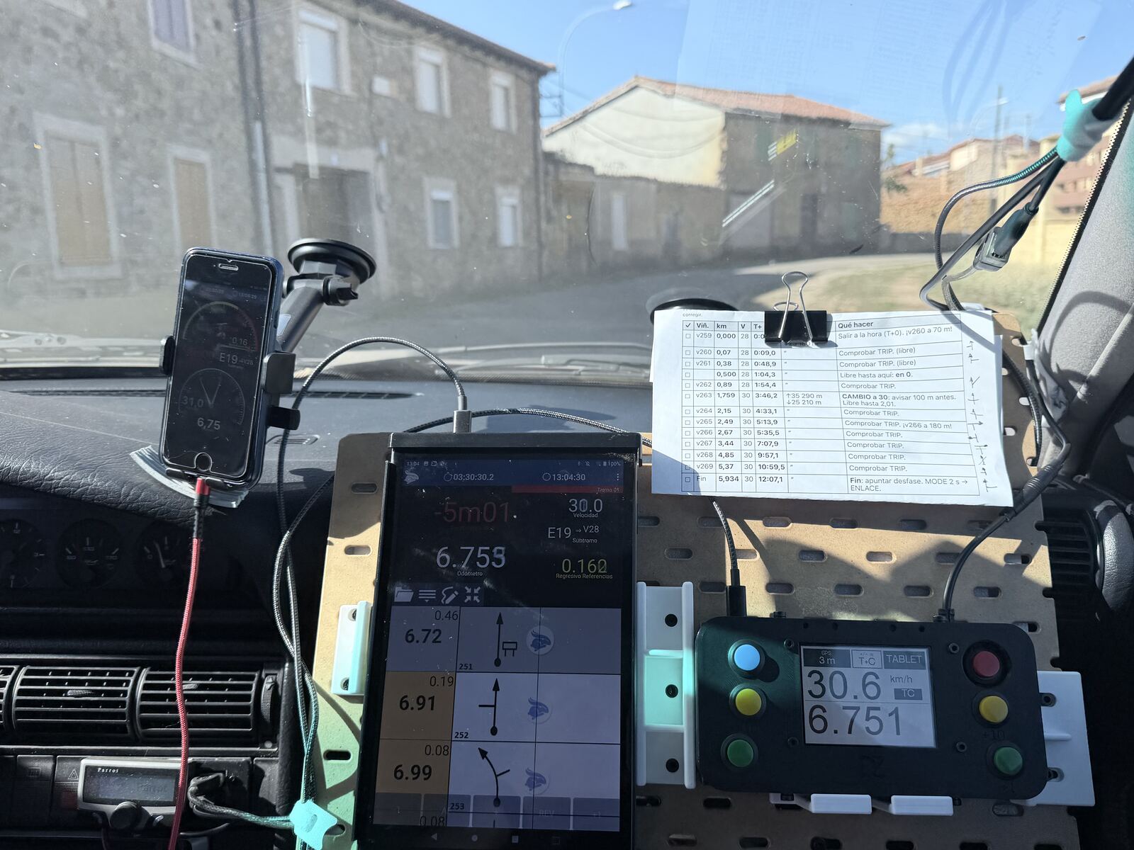 The panel during the race: the tablet with the roadbook tulips, the cockpit reading 30.6 km/h and 6.751 km, and a printed sheet of passing times held with a binder clip at the top right