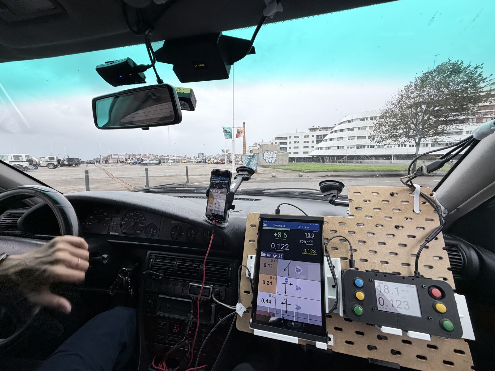 Inside the Audi at the start in Gijón: the SKÅDIS panel on the dashboard with the tablet showing the navigation app and the cockpit box reading 0.123 km, a phone on a suction mount and the neopod at the top of the windscreen